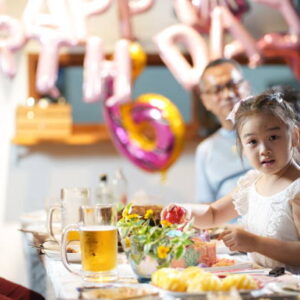 Cheerful young Asian girl cutting birthday cake among multi-generation family celebration for her birthday in the backyard